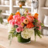 Mixed pink and orange flower arrangement in a green glass vase
