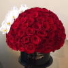 Round hatbox of densely packed red roses with a side accent of white orchids in a black container.