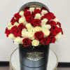 Round hatbox arrangement of red and white roses in a black box on a small table