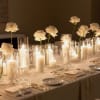 White flowers in glass cylinders with lit candles on a banquet table