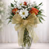 Bouquet of orange roses and white daisies in a clear glass vase with a gold bow
