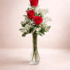 Three red roses arranged in a clear glass vase with white filler flowers