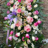 Tall standing spray of pink and white roses, lilies, and daisies with a lavender ribbon on an easel