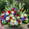 Tall red, white, and blue arrangement with roses, lilies, irises, and a patriotic ribbon in a rectangular container