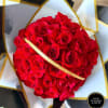Round bouquet of tightly clustered red roses wrapped in white and black paper with gold accents.