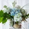 Blue and white flowers arranged in a glass vase with broad green leaves