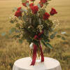 Red roses in a glass vase with greenery and a burgundy ribbon