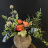 Mixed bouquet with orange roses, lilies, and blue flowers in a rustic vase