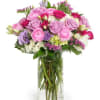 Tall glass vase of pink and lavender roses with mixed pastel flowers in a rounded arrangement