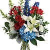 Bouquet of red roses, white lilies, blue flowers, and white snapdragons in a glass vase