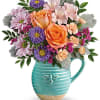 Bouquet of peach roses, pink daisies, and purple flowers in a turquoise pitcher vase