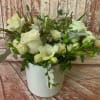 White floral arrangement in a white vase with roses and orchids