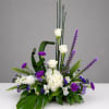 Tall floral arrangement with white roses, purple flowers, and tropical leaves