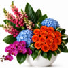 Mixed bouquet in a white bowl vase with orange roses, blue hydrangeas, pink snapdragons, and purple orchids