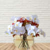 White orchid arrangement in a round glass vase with red berry accents