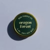 Round green candle tin labeled Oregon Forest