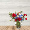 Bouquet of red roses, blue hydrangeas, and white blooms in a glass vase