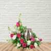 Pink roses and white flowers arranged around a silver urn