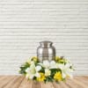 White lilies and yellow flowers arranged around a silver urn