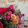 Handheld bouquet of pink, peach, and purple roses with mixed blooms