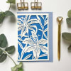 Blue floral cutout card with white lily design and a gold pen