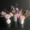 Three small pink floral arrangements in white vases on a dark surface
