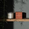 A scented candle in a frosted glass jar beside its coral box