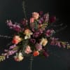 Moody arrangement of peach roses, white daffodils, and purple tulips on a dark background