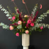 Tall arrangement of pink roses, berries, and burgundy accents in a white ribbed vase with sweeping eucalyptus.