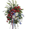 Standing floral spray with red carnations, white lilies, and blue flowers on a tripod stand