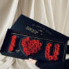Red roses arranged in a heart and the word LOVE in a black gift box