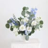 White and blue flowers arranged in a white vase with round eucalyptus leaves