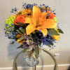 Bouquet of orange lilies, roses, and blue filler flowers in a glass vase