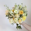 Handheld bouquet of pale yellow and white flowers with small daisy accents