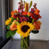 Mixed bouquet of sunflowers, roses, and orange blooms in a glass vase