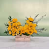 Yellow flowers arranged in a wooden box with eucalyptus accents