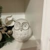 White ceramic owl figurine on a shelf beside holiday greenery