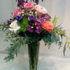Tall mixed bouquet of roses, irises, and purple flowers in a clear glass vase