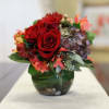 Red roses and hydrangeas arranged in a green glass vase