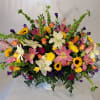 Large mixed bouquet with lilies, roses, sunflowers, and purple accents in a clear vase