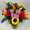Bright mixed bouquet with sunflower, red roses, orange lilies, and purple mums in a clear glass vase