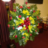 Large standing floral spray with yellow lilies, red roses, and a red ribbon