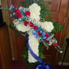 Cross-shaped floral tribute with white carnations, red roses, and blue flowers