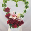 Heart-shaped floral arrangement with red roses and pink lilies in a white container
