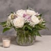 White rose bouquet in a glass vase with a small candle beside it