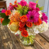 Bright mixed bouquet in a clear glass vase with pink, orange, and white flowers.