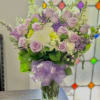 Lavender rose bouquet with white blooms in a clear glass vase and purple ribbon