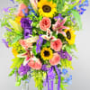 Tall standing floral spray with sunflowers, pink roses, lilies, and purple flowers on an easel