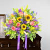 Bright casket spray with sunflowers, pink roses, lilies and purple blooms on a wooden casket