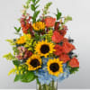 Sunflowers, orange roses, and blue hydrangeas in a clear glass vase